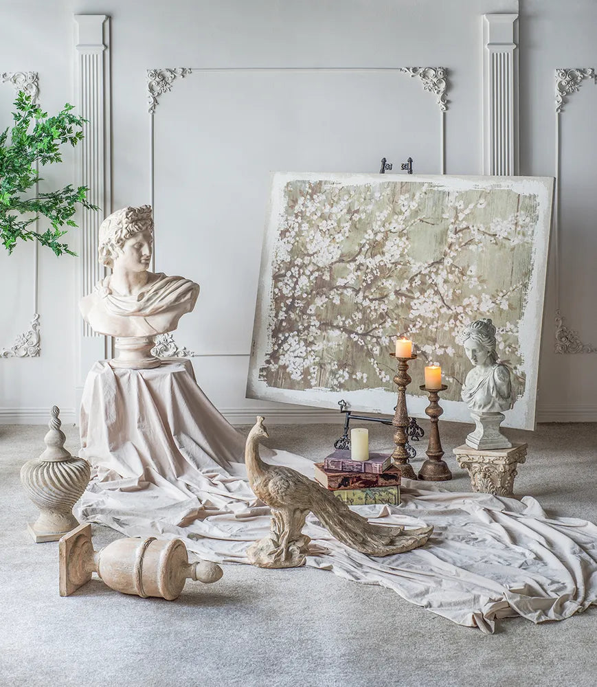Decorative setting with classical sculptures, peacock, and candles in a room with white walls and columns.