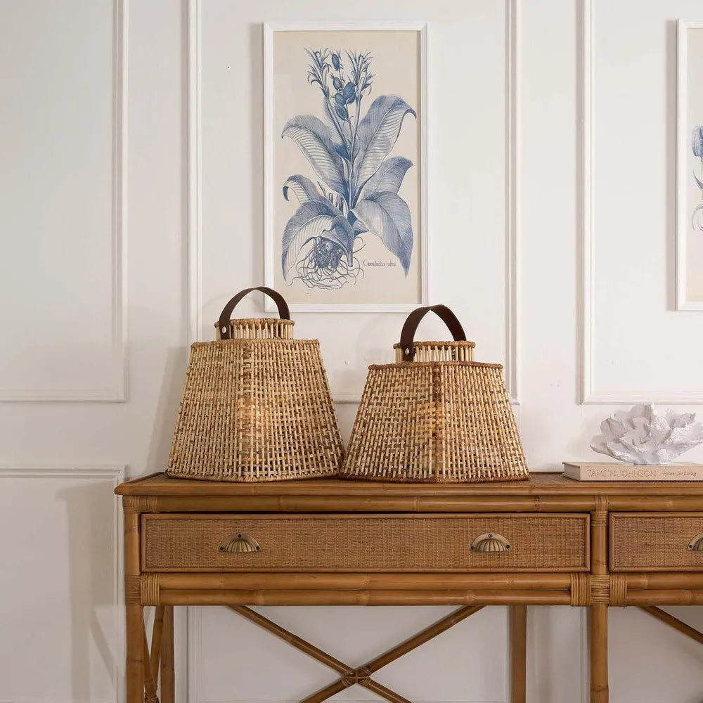 Wicker console table with two woven lamps and a framed botanical print on the wall.