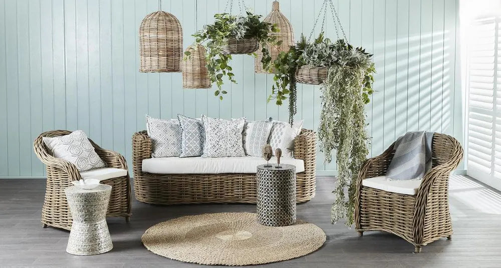 Outdoor furniture set with wicker chairs, sofa, and tables against a light blue wall.