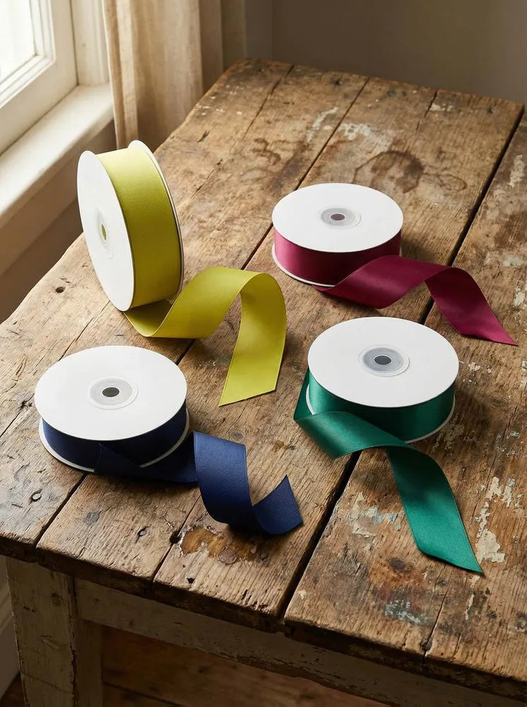 Four spools of ribbon in yellow, red, blue, and green on a wooden table.