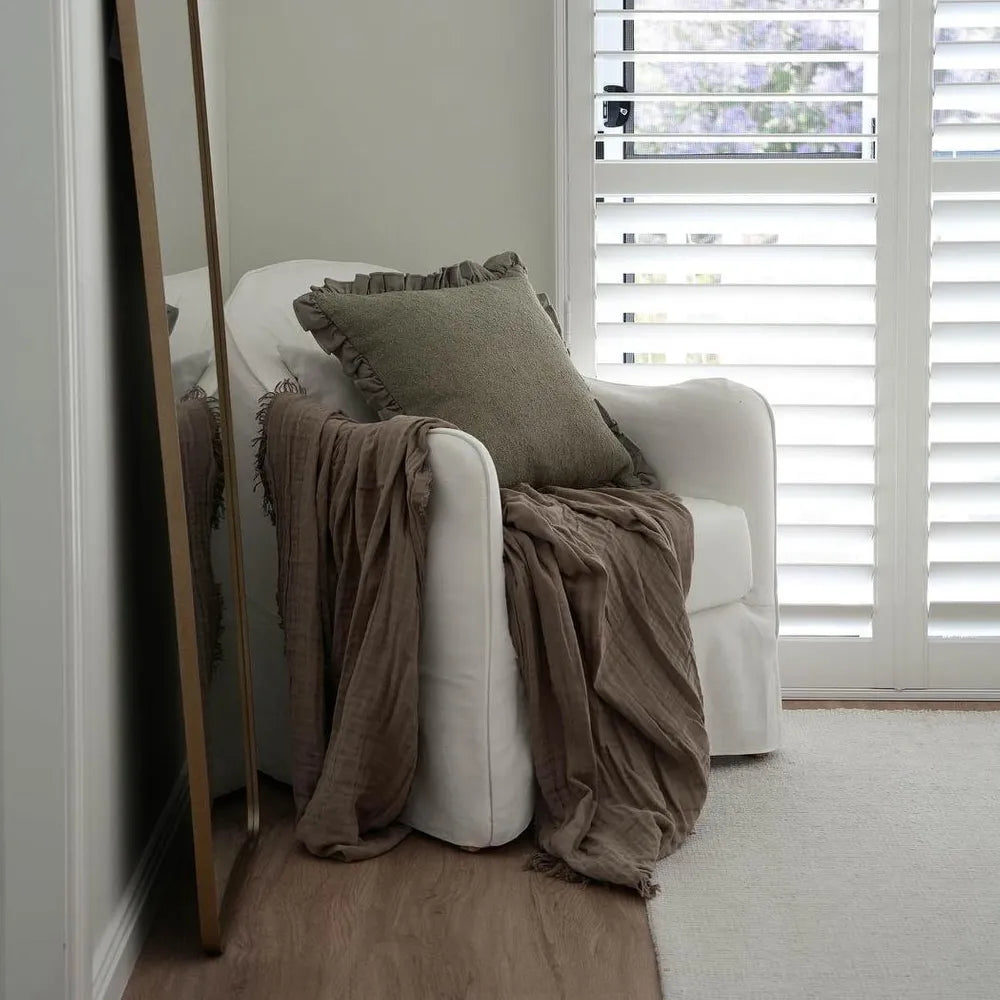 White armchair with brown blanket and pillow in a room with a window and mirror.