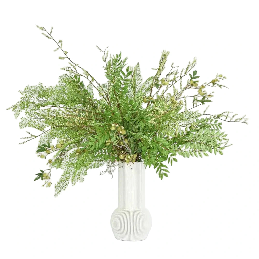 Green leafy arrangement in a white vase on a light blue background