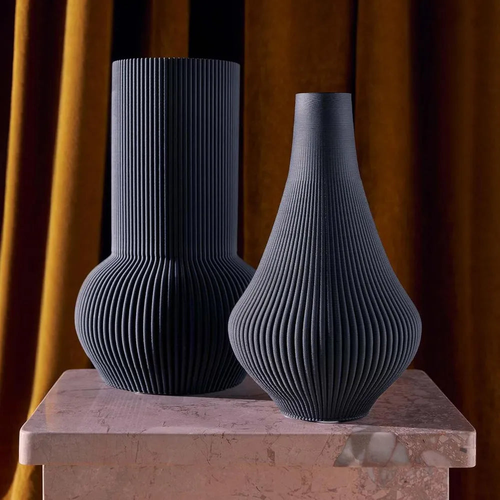 Two black textured vases on a marble surface with a warm brown curtain background