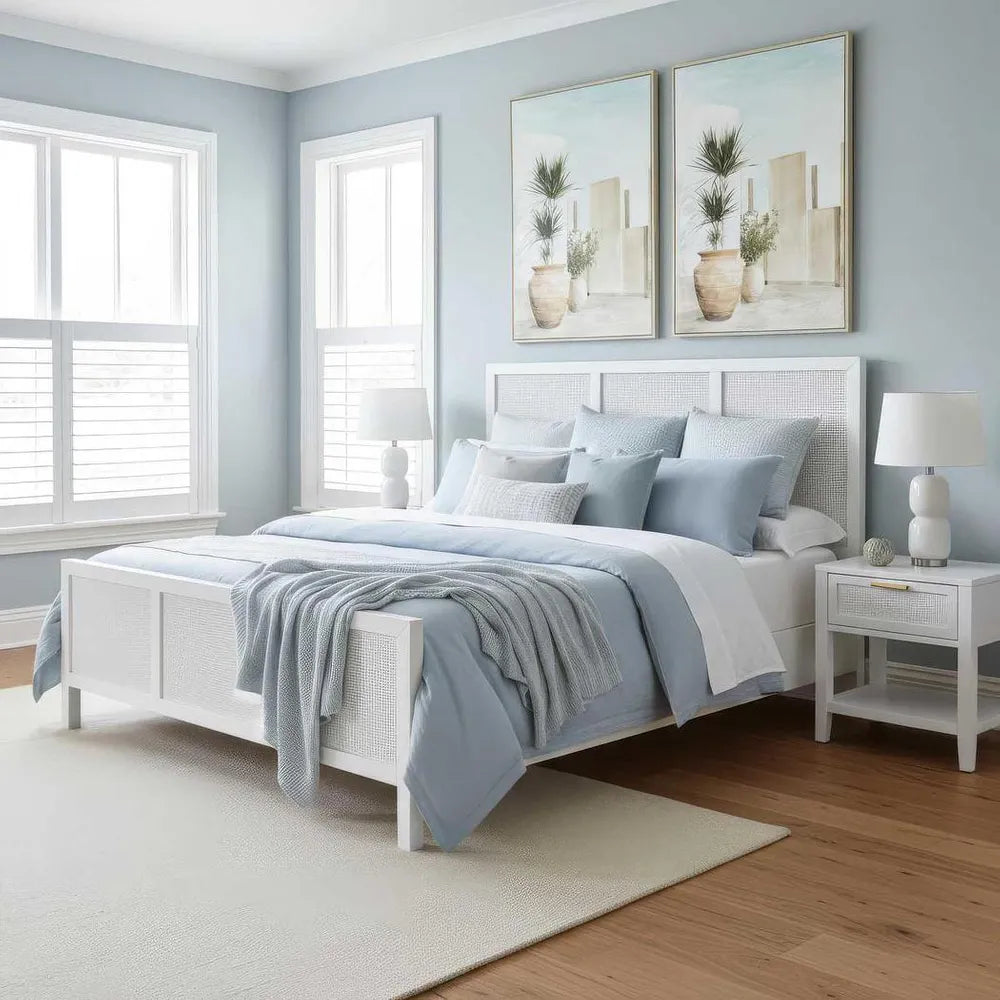 Neatly made bed with light blue bedding in a bedroom with light blue walls and white windows.